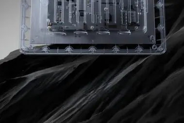 Przezroczysta obudowa punktu dostępowego Zyxel WBE665S, ukazująca wewnętrzne układy elektroniczne i płytę główną, umieszczona nad pofałdowaną, czarną strukturą przypominającą skały lub ciemną materię.