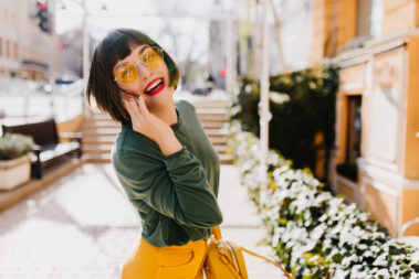 Lovable short haired girl in yellow sunglasses having fun outdoor and posing with pleasure. Portrai