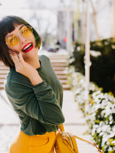 Lovable short haired girl in yellow sunglasses having fun outdoor and posing with pleasure. Portrai