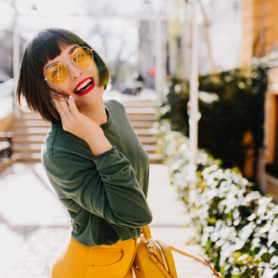 Lovable short haired girl in yellow sunglasses having fun outdoor and posing with pleasure. Portrai